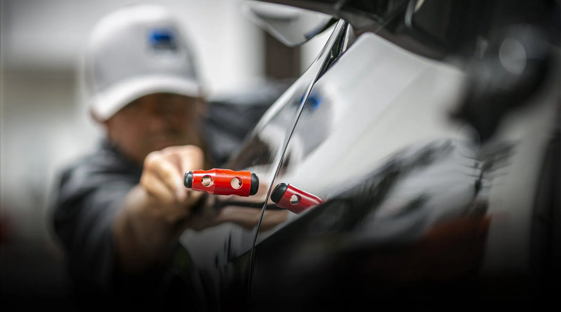 Paintless dent repair in progress — glue-pull tabs on a black panel, Calgary